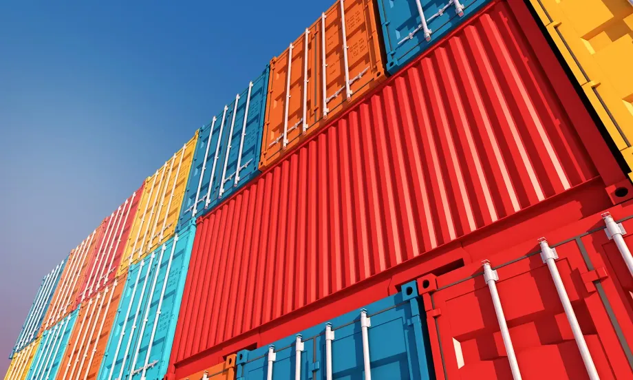 Stacked colorful shipping containers against a blue sky at a port