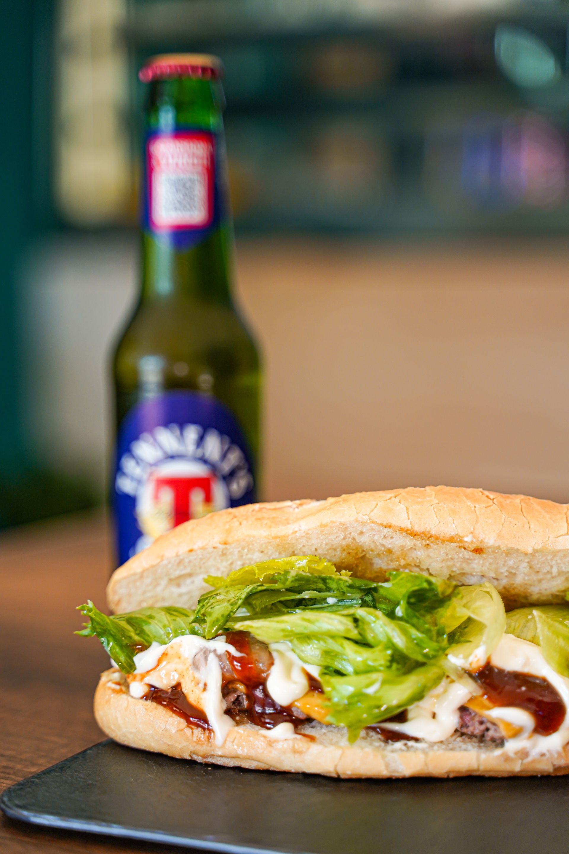 Panino con lattuga e salsa, accanto a una bottiglia di birra.