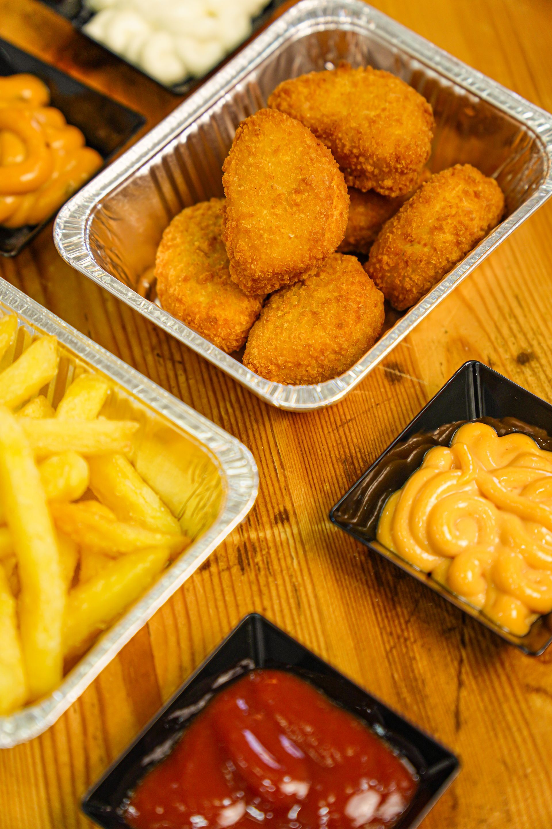 Nuggets di pollo fritti e patatine fritte con salse su un tavolo di legno.