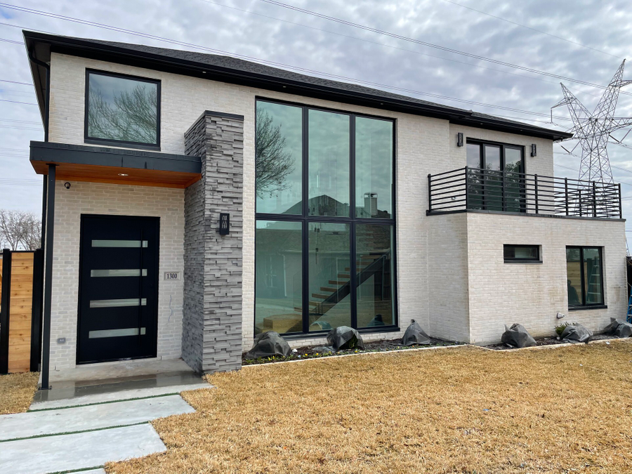 Modern two-story house with large windows, black front door, stone accents, and a balcony on a snowy lot