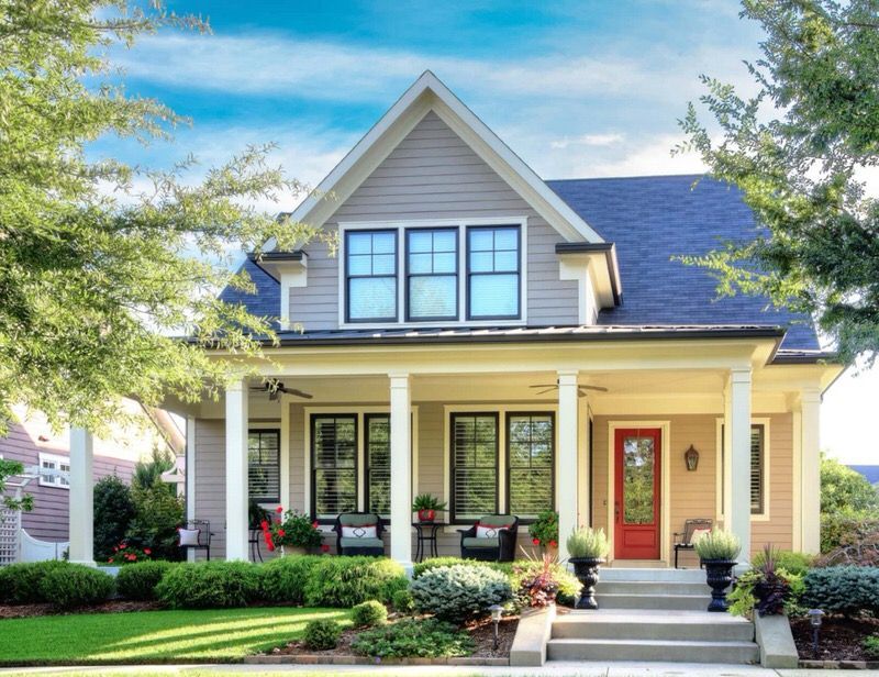 Charming cream-colored house with a front porch, blue roof, and landscaped yard on a sunny day