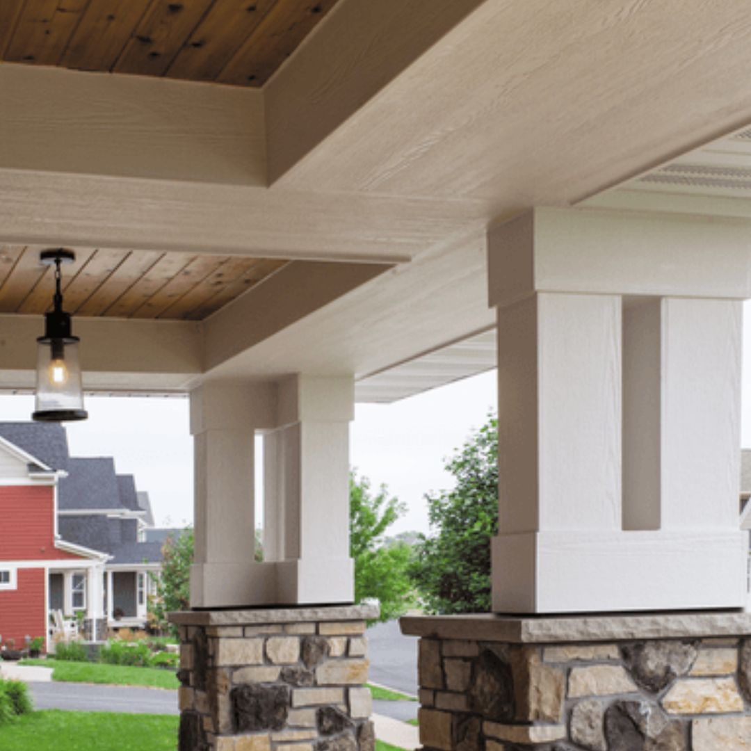 Covered front porch with white columns, stone bases, and a view of neighboring houses and greenery.