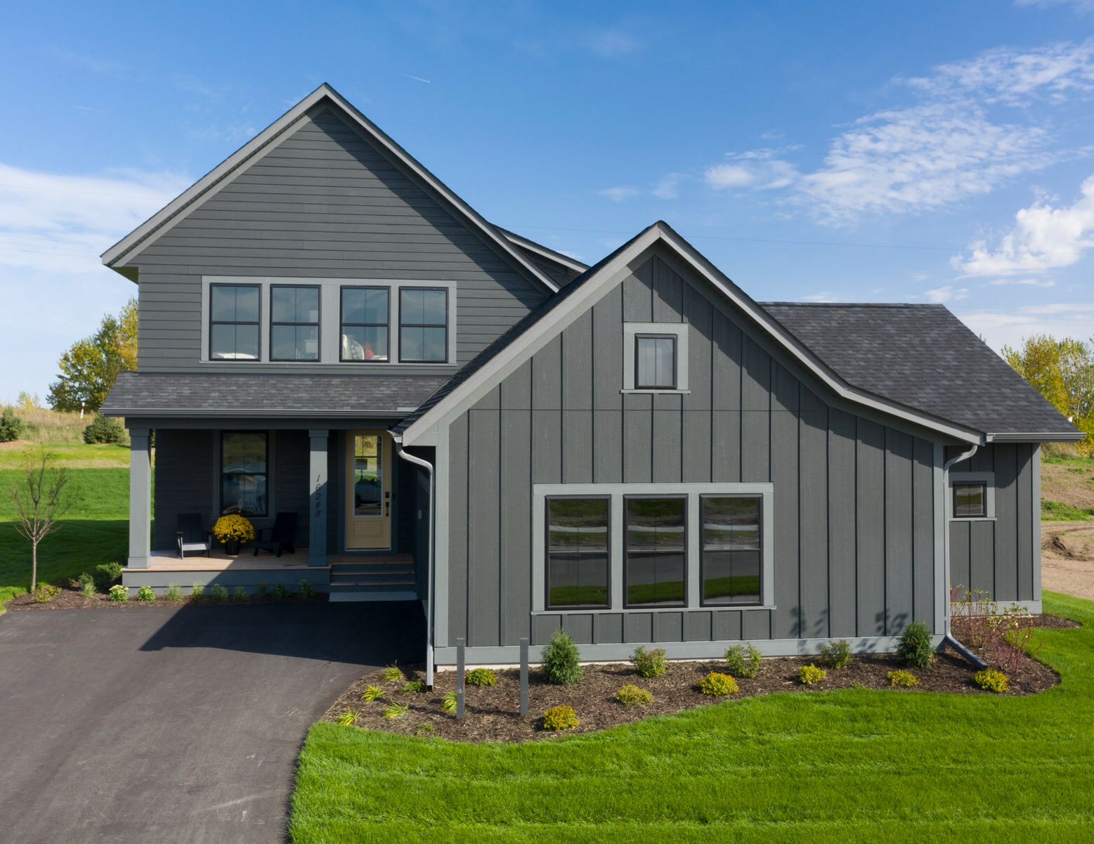 Modern gray two-story house with gabled roof, black driveway, and green lawn under a blue sky