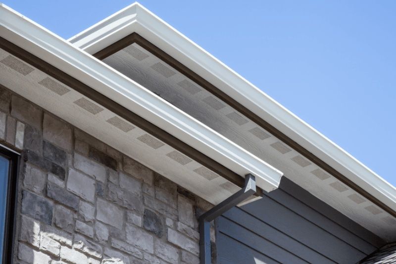 Stone house eaves and white gutter against a blue sky