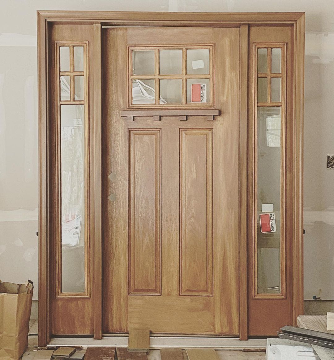 Wooden front door with sidelights and a small transom window in a beige wall