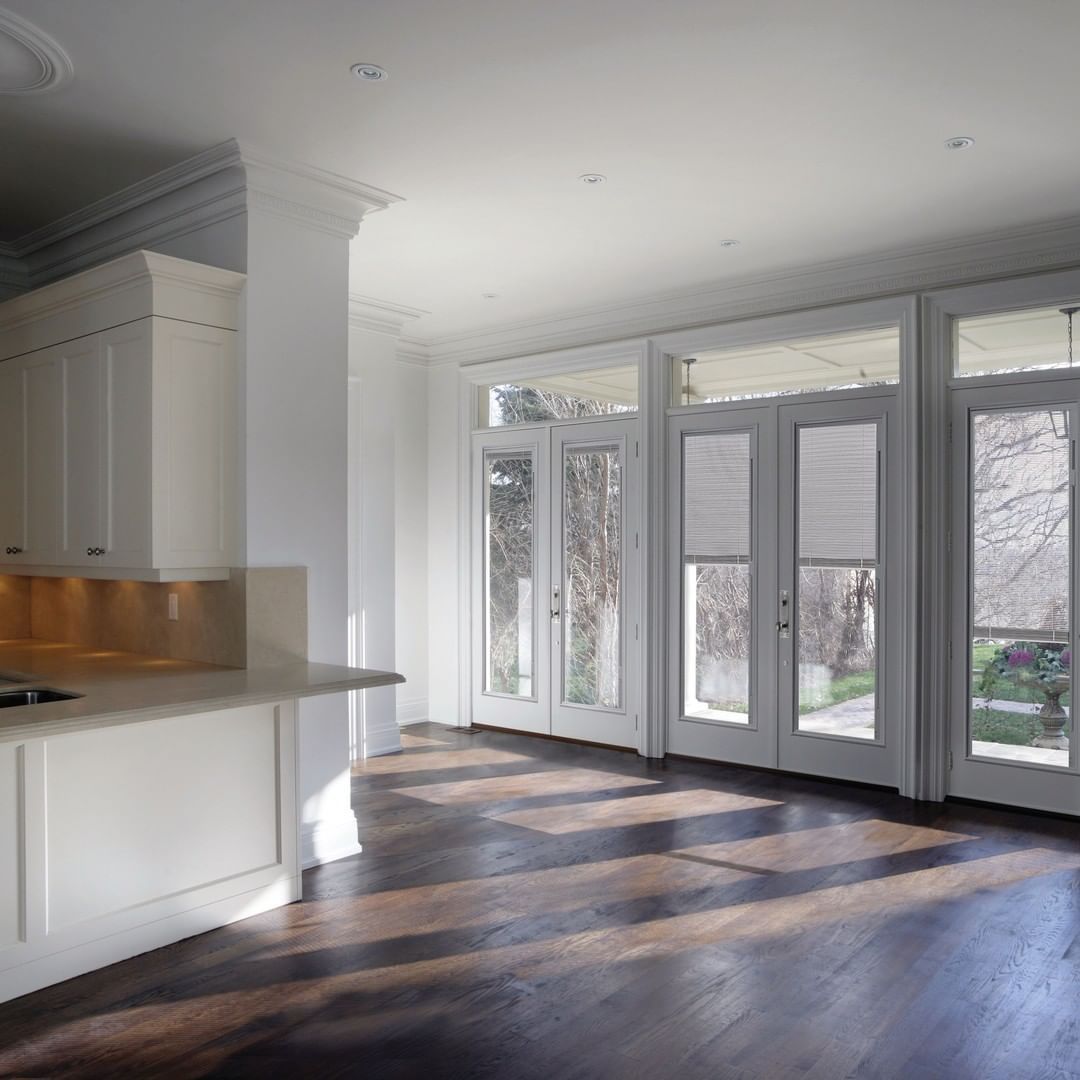 Bright modern kitchen-living space with white cabinets, dark wood floors, and large glass doors opening to snowy outside