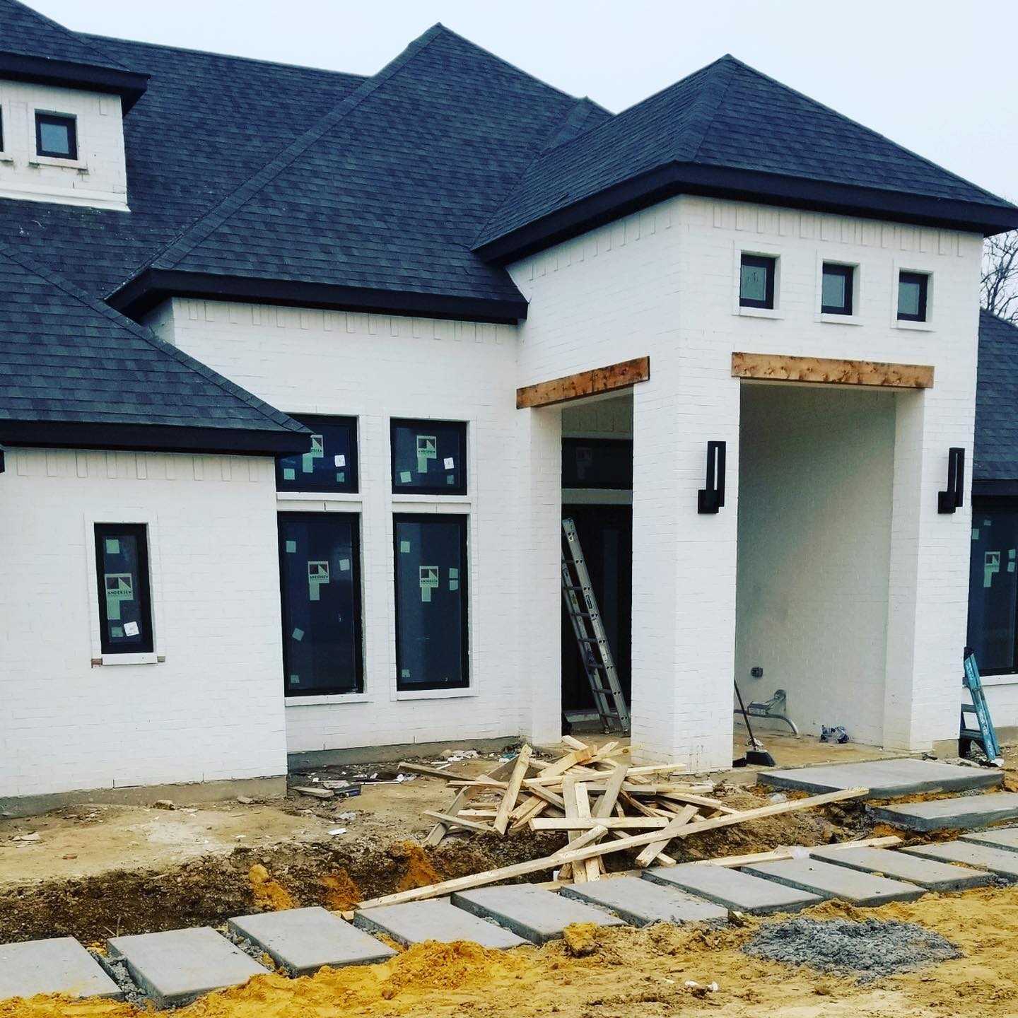 New white house under construction with dark roof, front porch, and unfinished yard