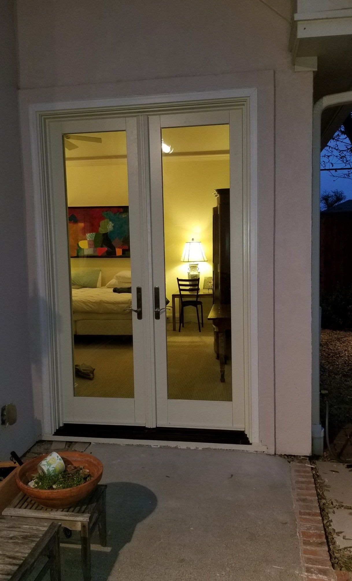 Open double glass doors showing a warmly lit interior with a bed and lamp at dusk.