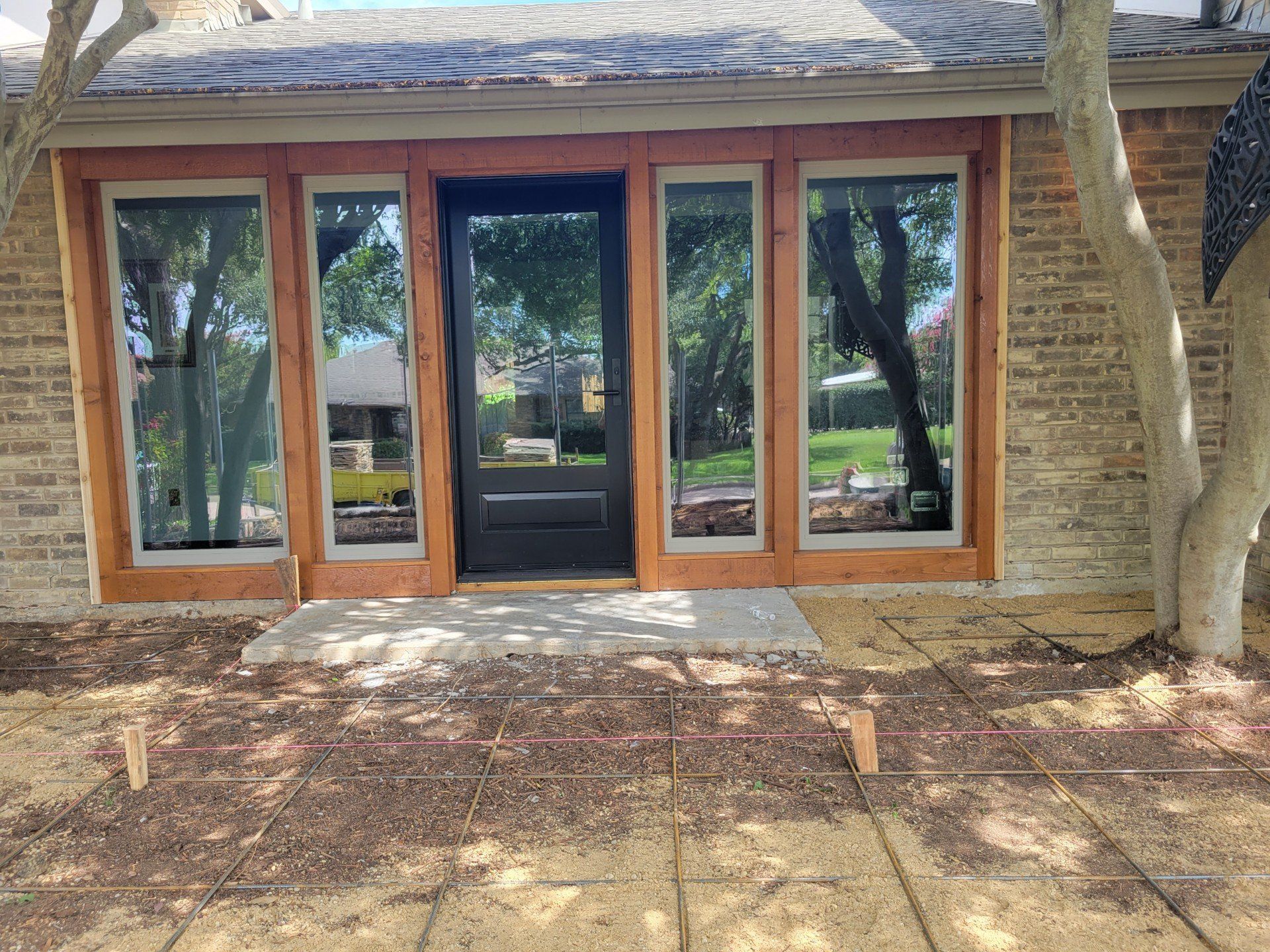 Front view of a brick house entrance with double wooden doors and large windows, beneath a shaded porch