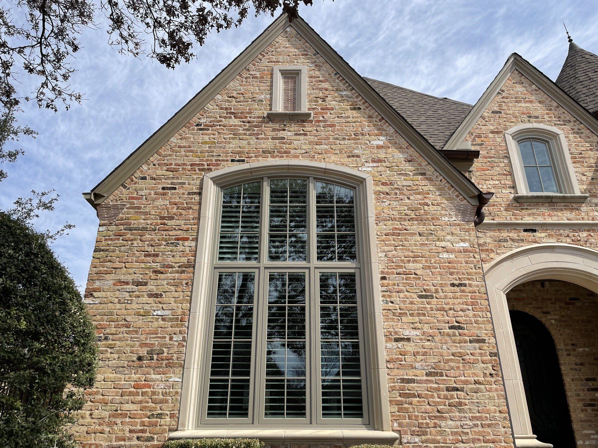 Brick house facade with a tall arched window and peaked roof against a blue sky