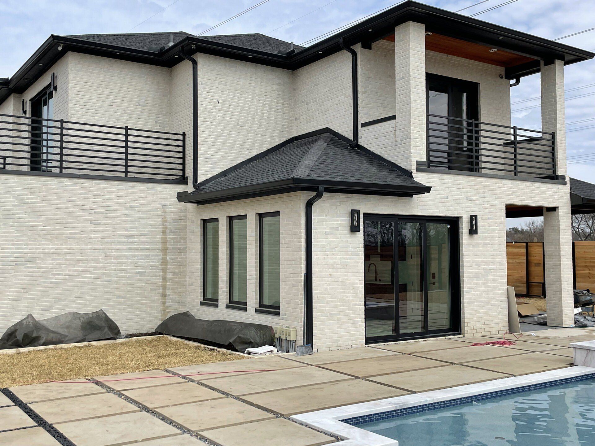 Modern two-story house with a pool, white brick exterior, and black roof by a patio