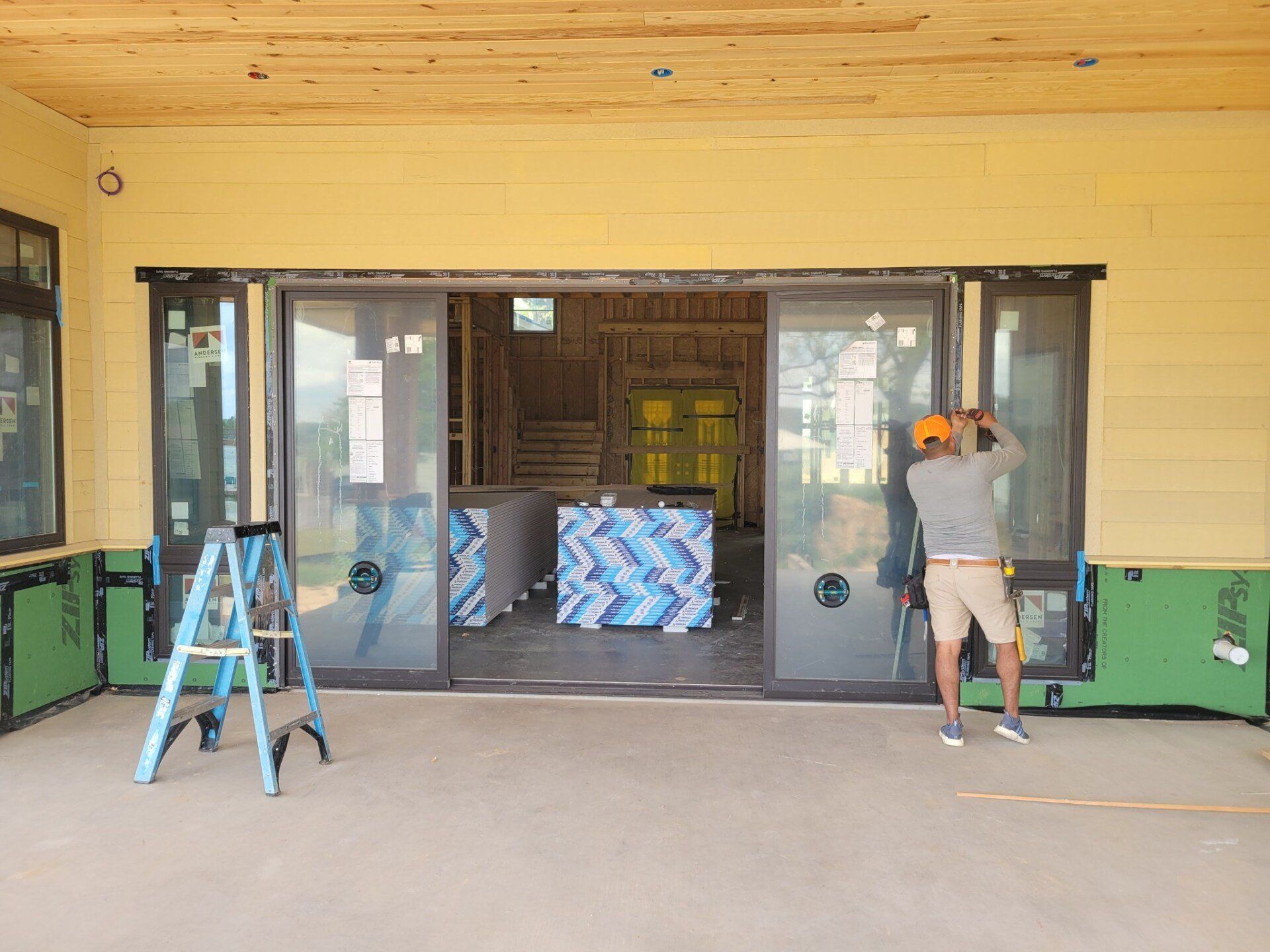 Two workers install sliding glass doors on a covered porch, with tools and materials nearby.