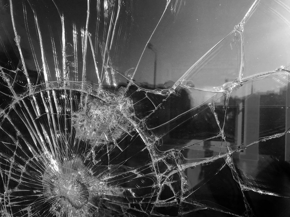 Shattered car windshield with spiderweb cracks and a large impact hole on the left side.