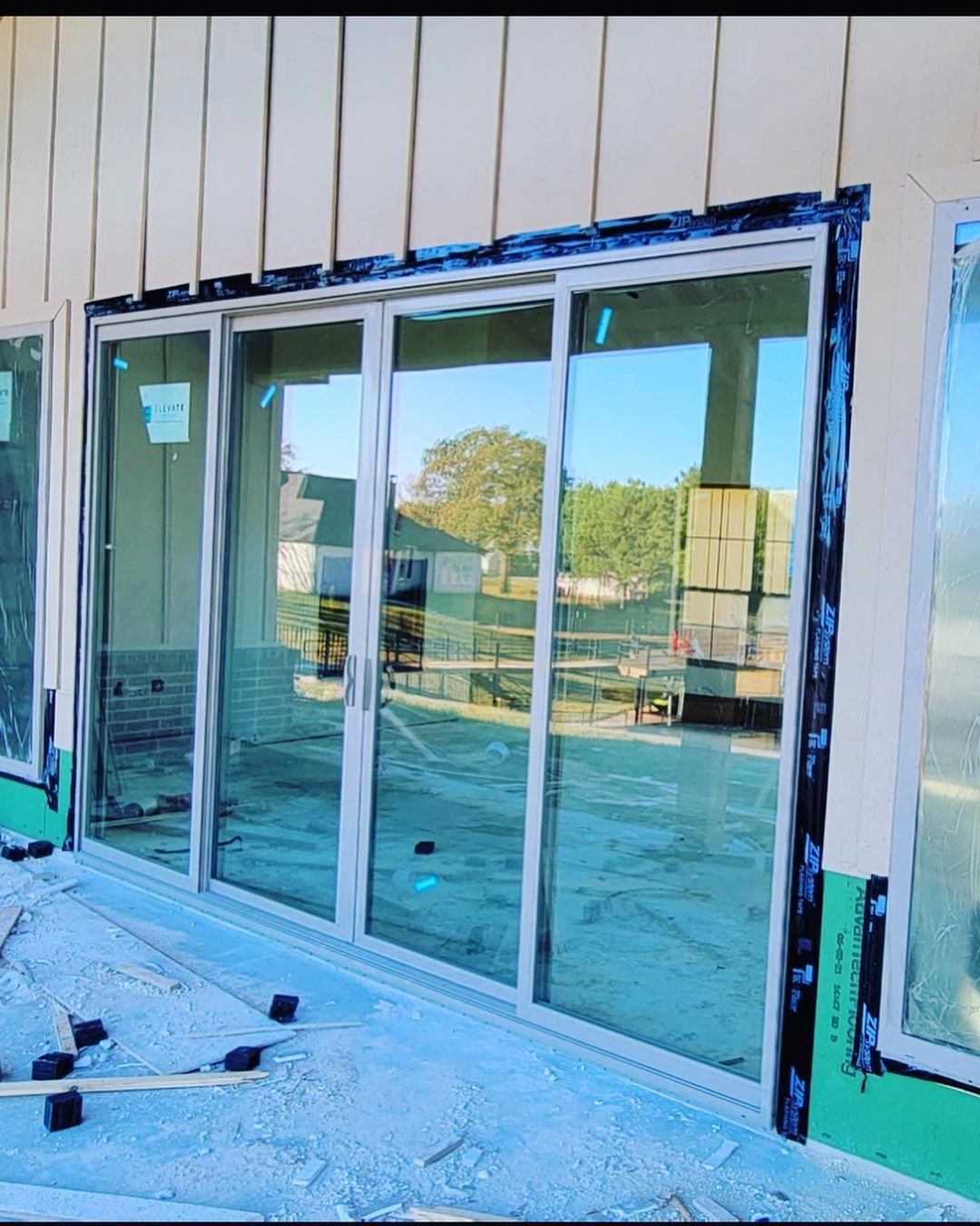Sliding glass doors at a building entrance, with construction debris on the ground.
