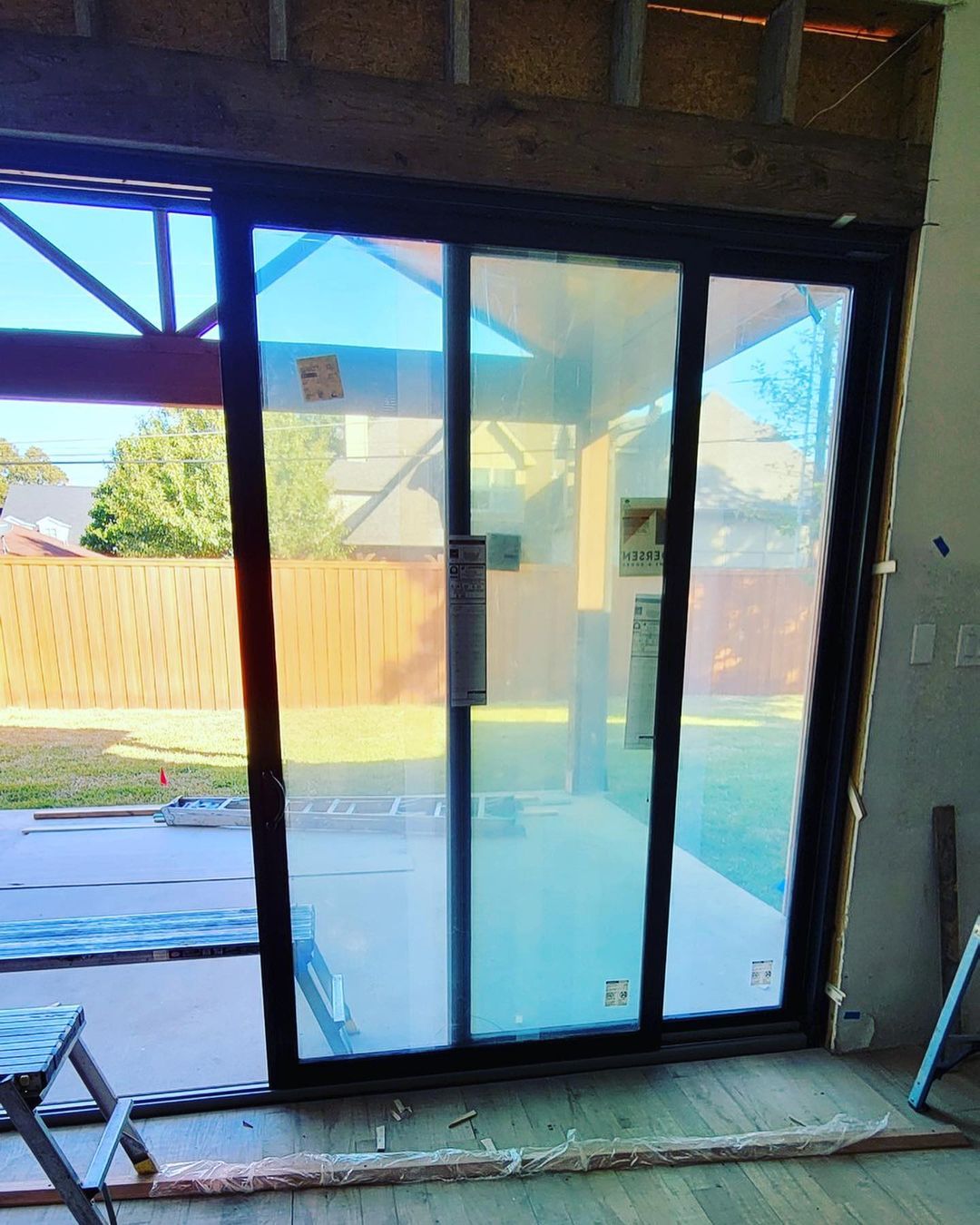 Sliding glass door opening to a backyard patio with a wooden fence and blue sky outside