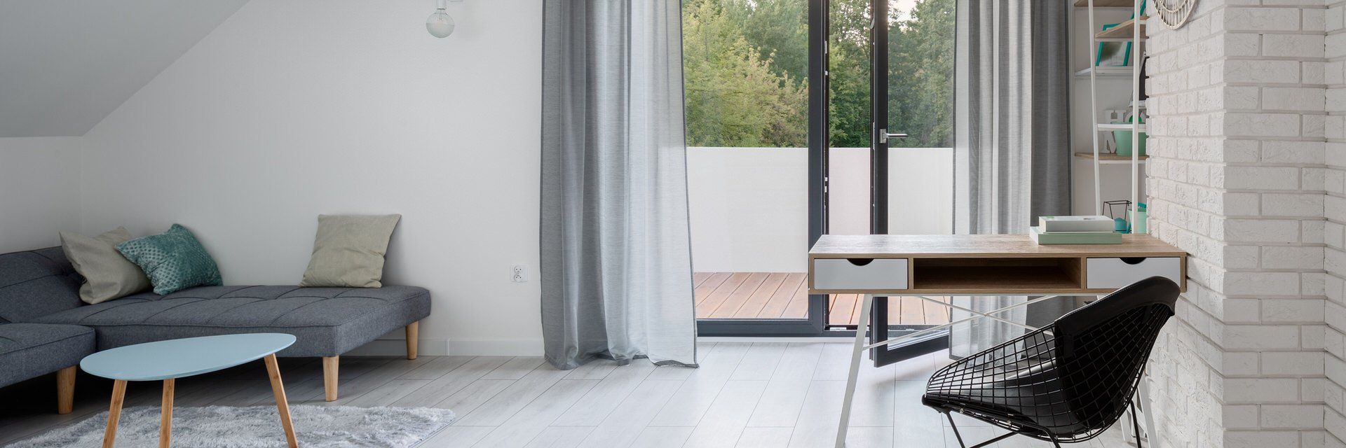 Minimalist living room with gray sofa, round coffee table, desk, and black chair by large windows
