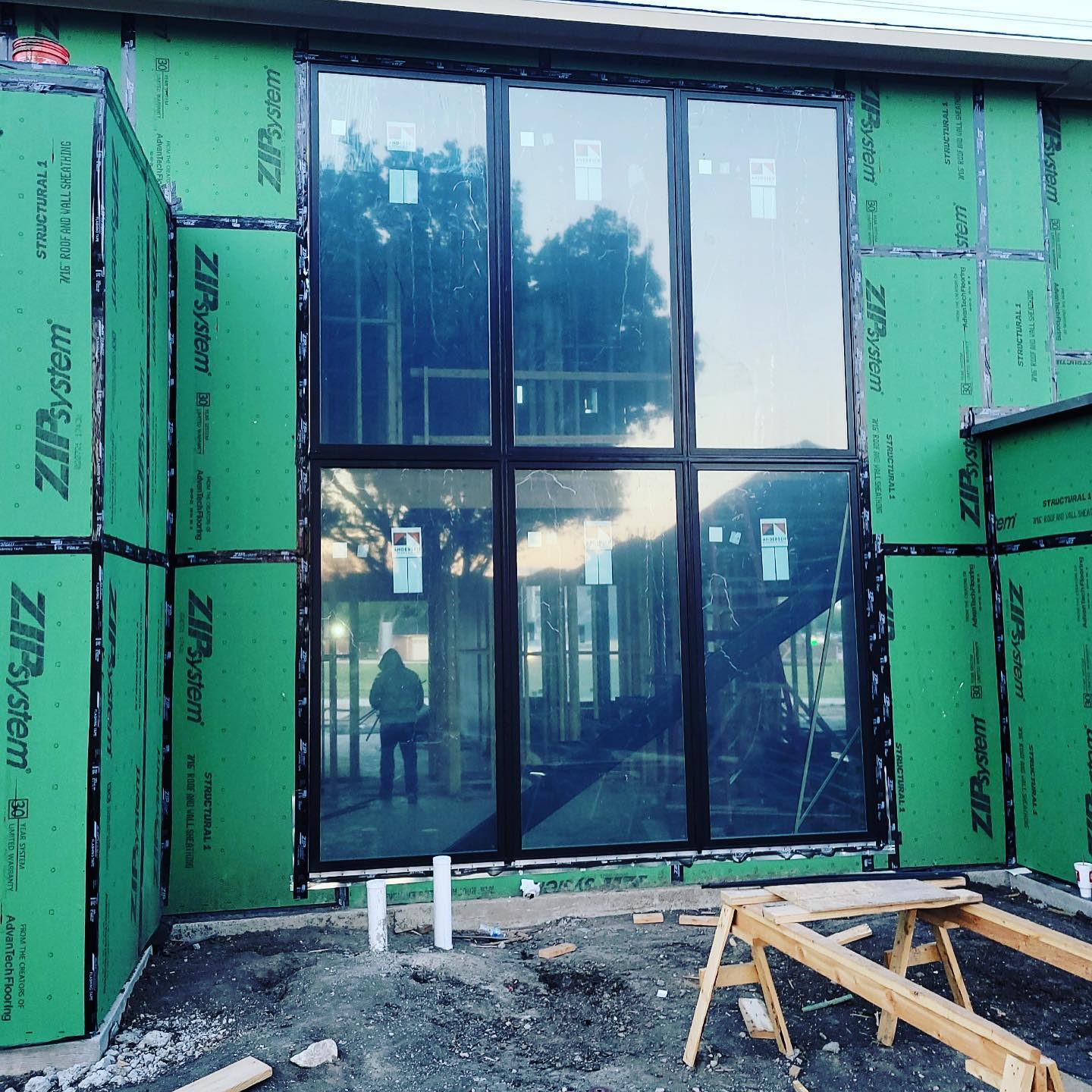 Modern house exterior under construction with green insulation panels and large black-framed windows
