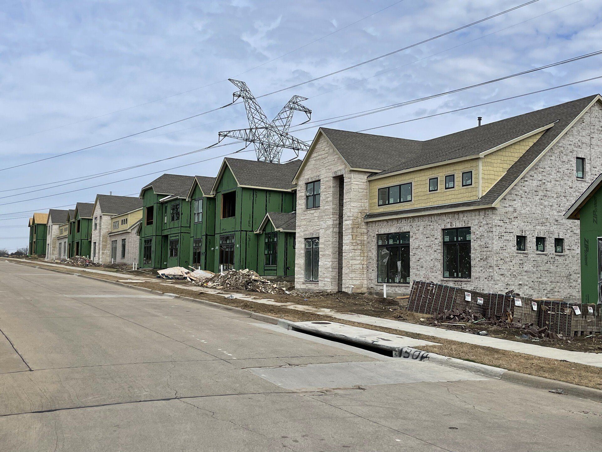 Row of new townhouses with green and gray siding along a quiet street under a cloudy sky