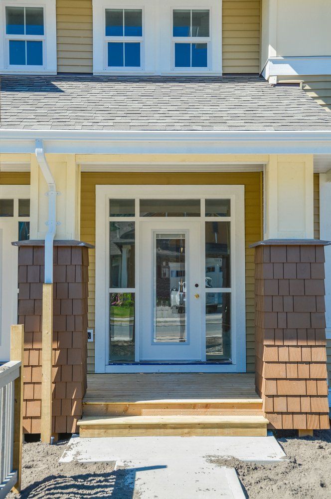 Front entrance of a house with white double doors, tan siding, and brick columns