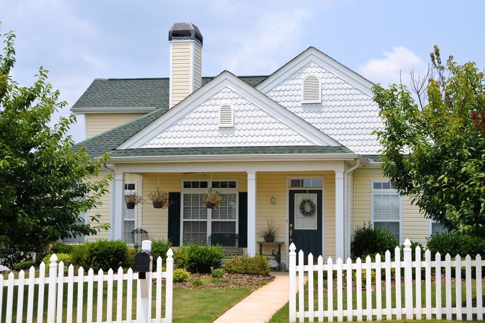 White house with front porch, picket fence, and green lawn under a clear sky
