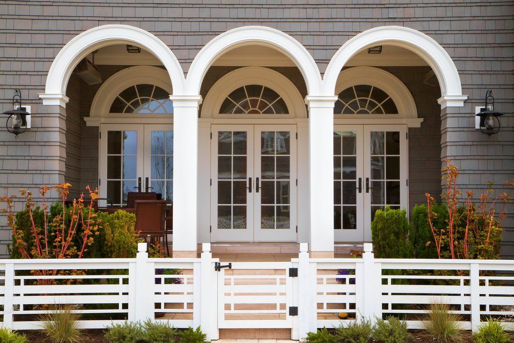 White arched porch with glass doors, windows, and a white fence in front of a gray house.