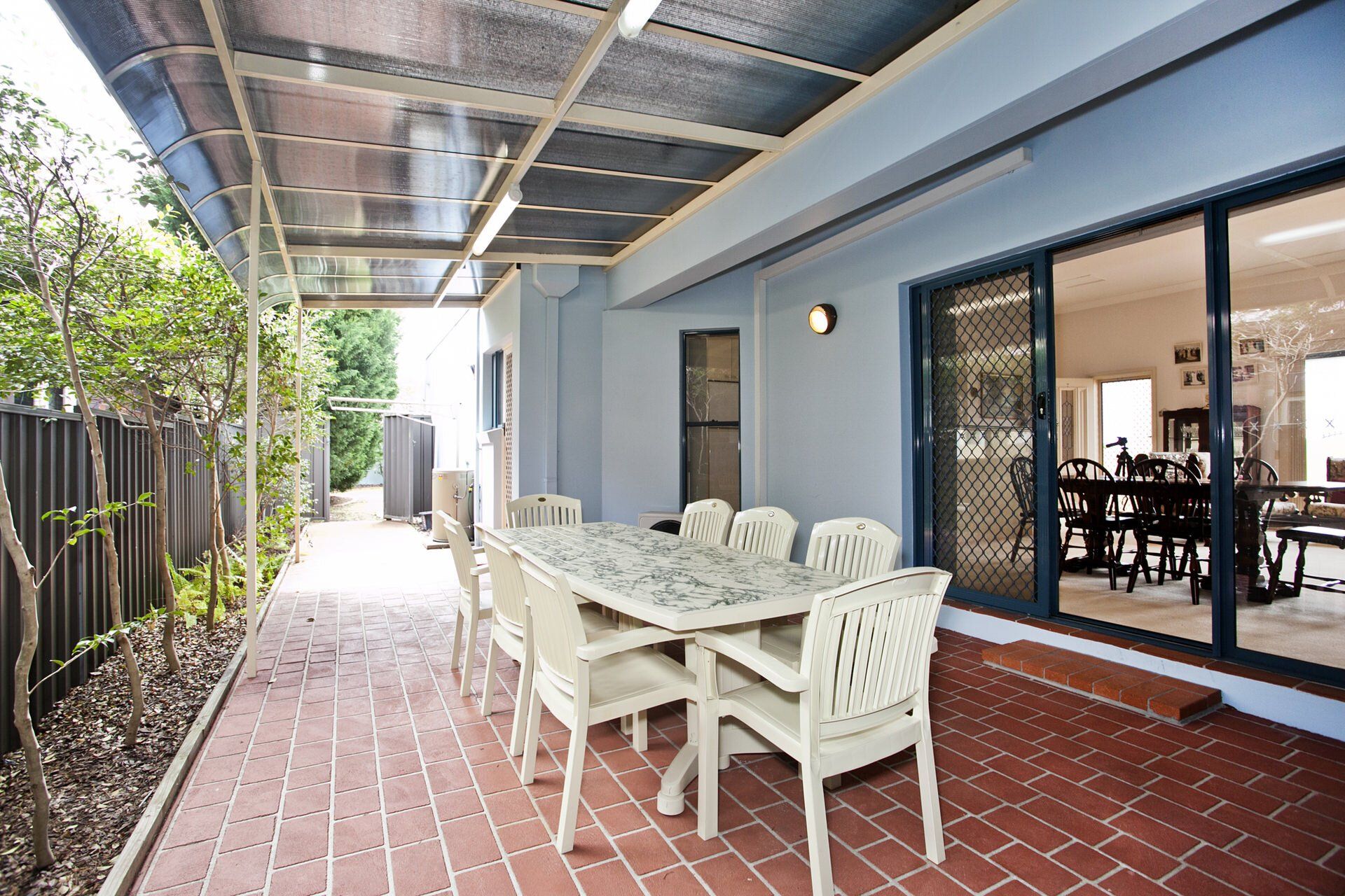 Covered patio with white dining table, brick floor, and glass doors opening to an indoor dining room