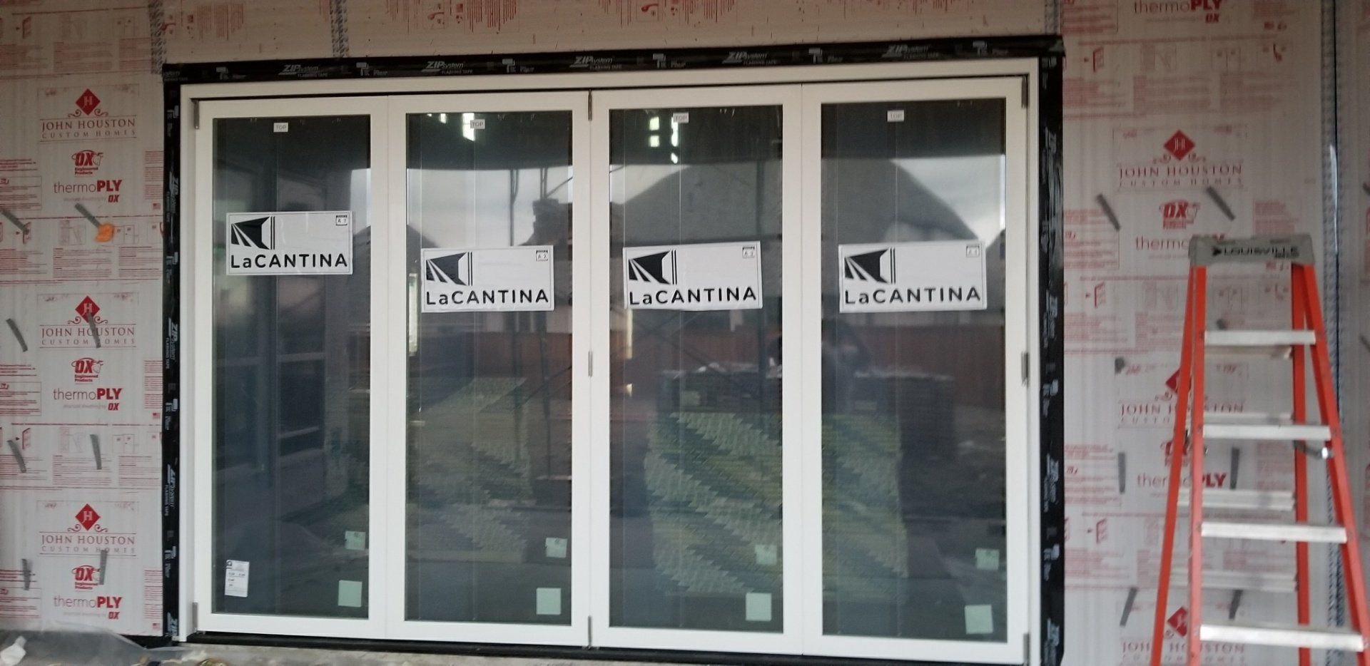 Four-panel glass storefront under construction, with orange ladder and insulation-covered walls