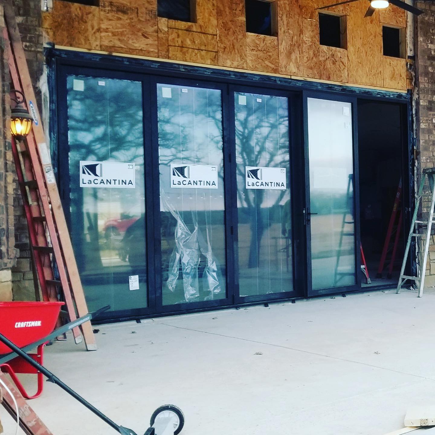 Storefront under construction with black glass doors, plywood framing, and ladders on either side.