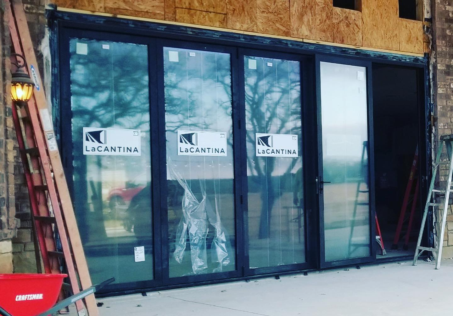 Storefront with large dark-framed glass doors and windows under construction, with scaffolding nearby.