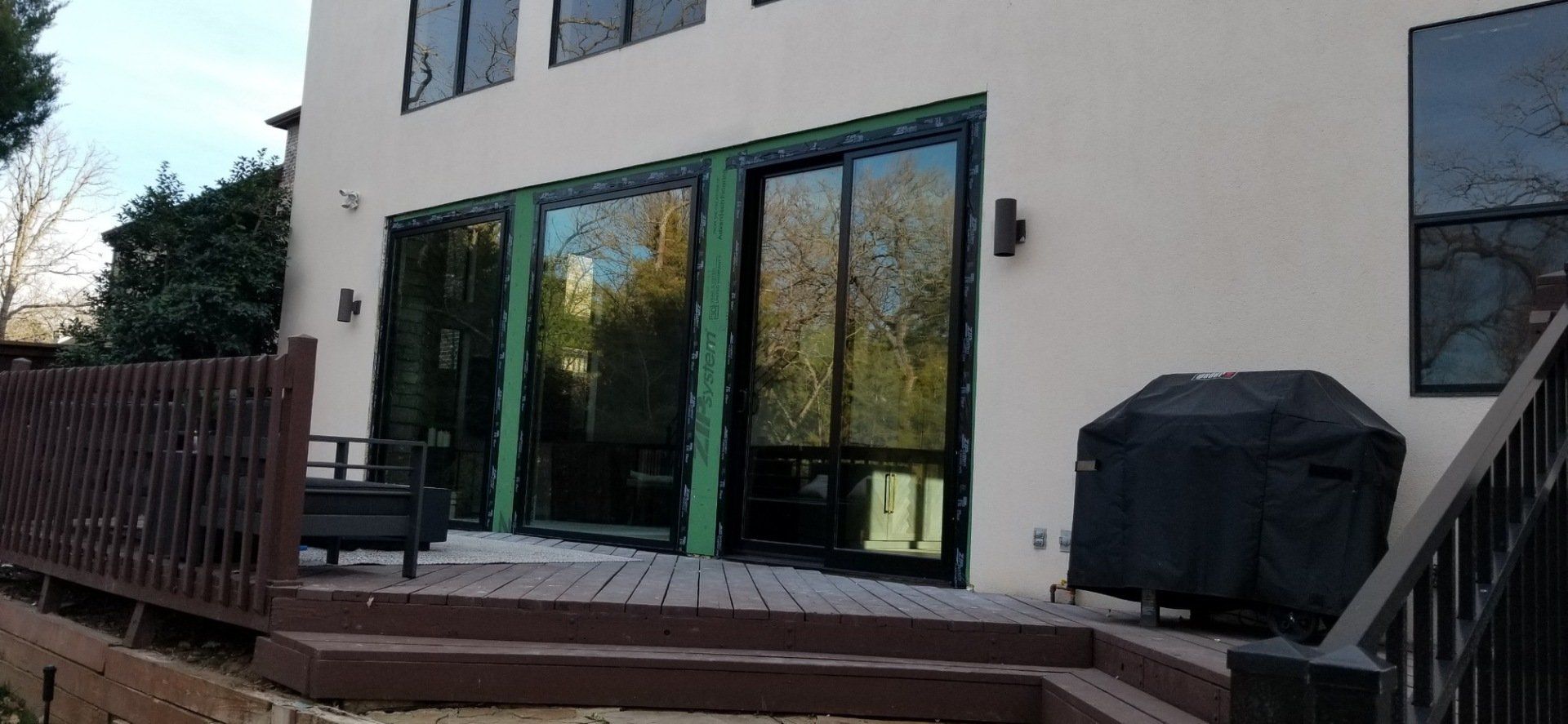 Patio with glass sliding doors on a house, wooden deck, and covered grill beside stairs