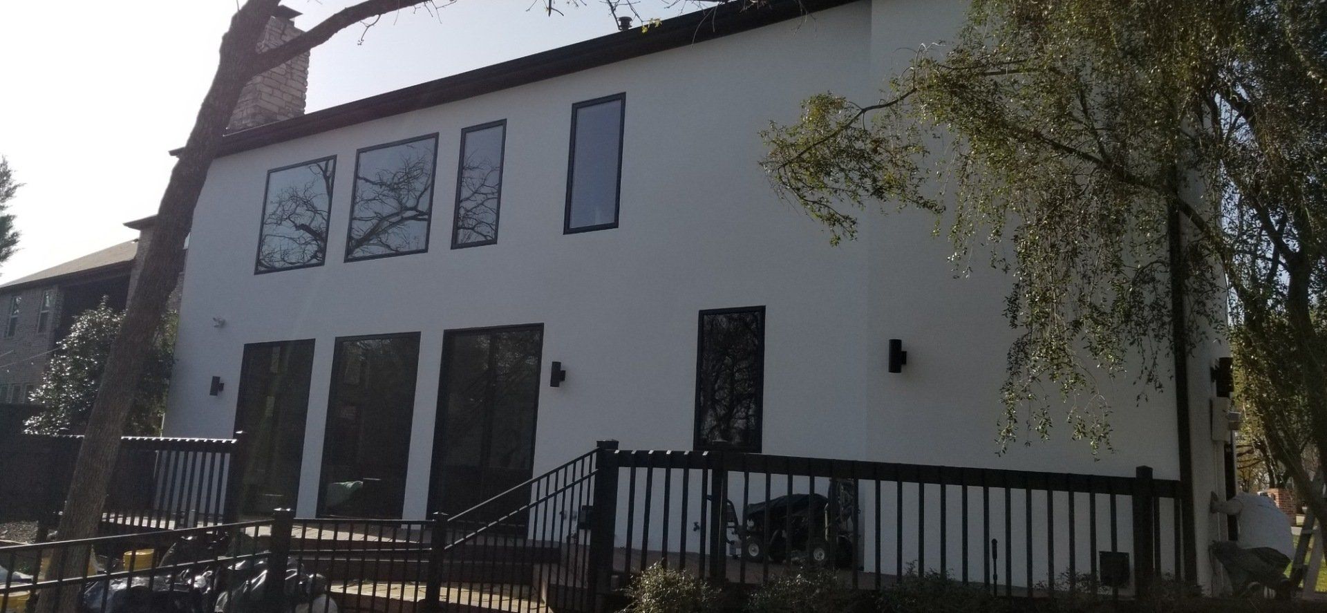White two-story house with black-trim windows and a fenced front yard in sunlight