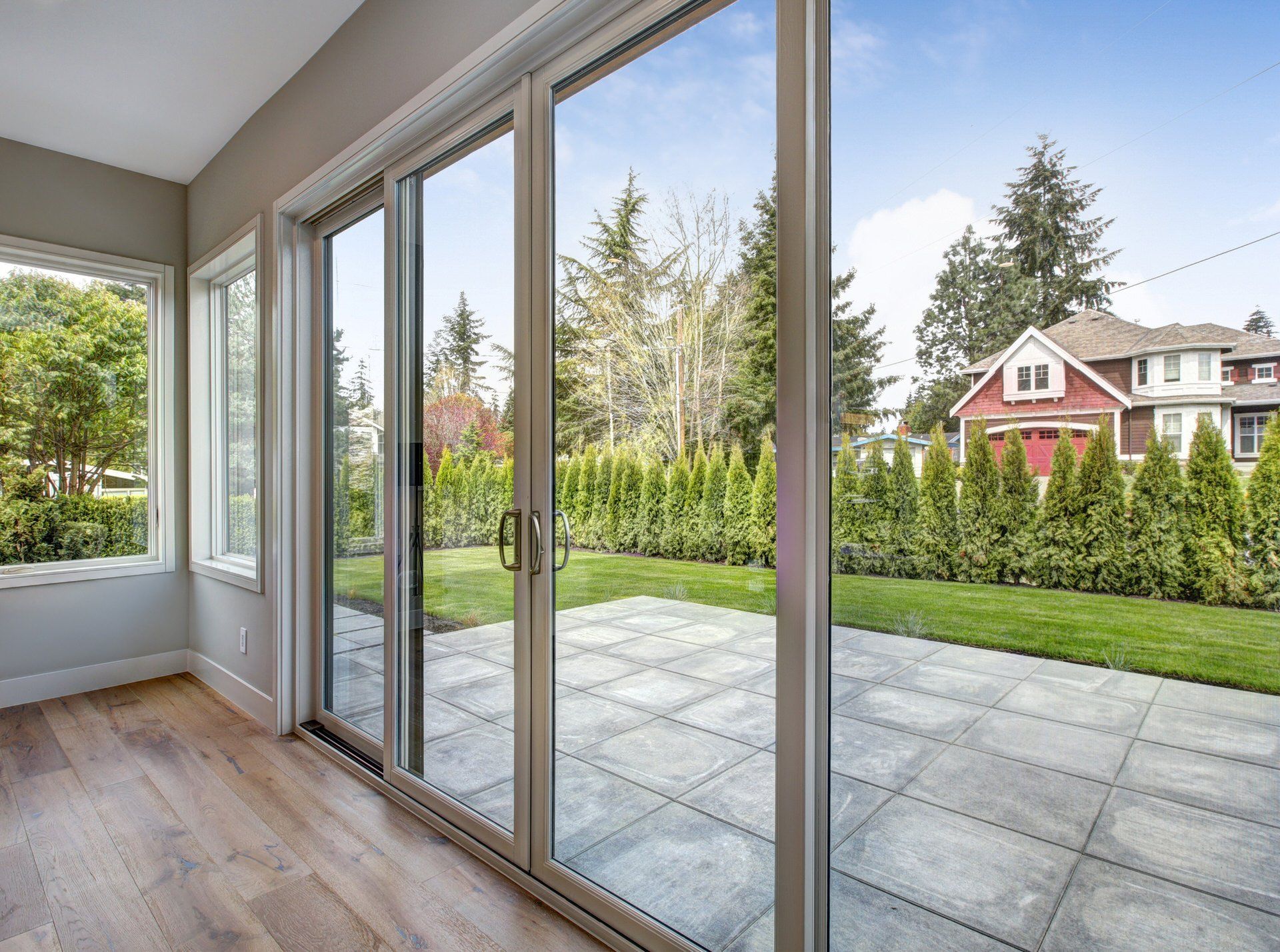 Sliding glass doors opening to a patio and green backyard with a red house beyond.