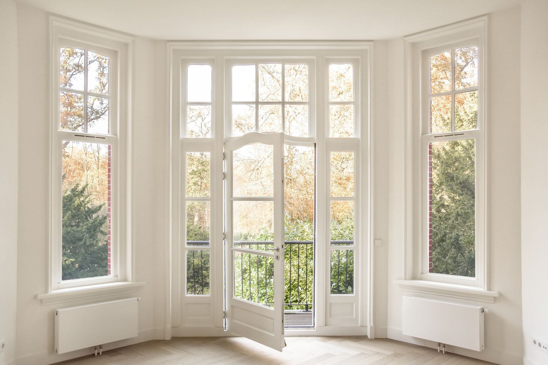 Bright bay window alcove with white trim, glass doors, and autumn trees outside