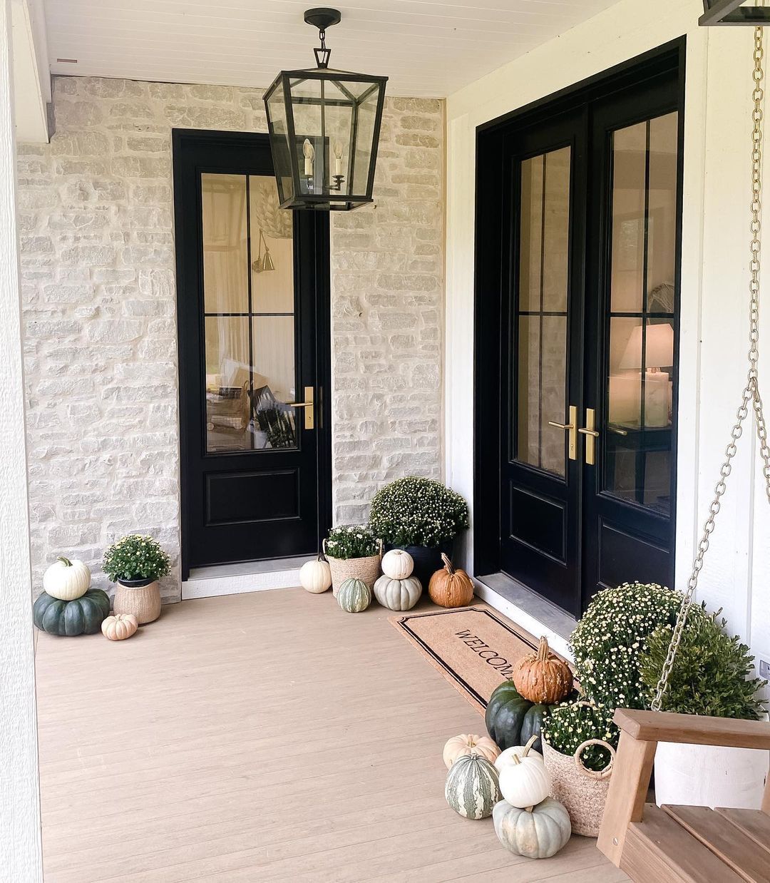 Covered front porch with black doors, white brick walls, lantern light, and pumpkins by the entrance