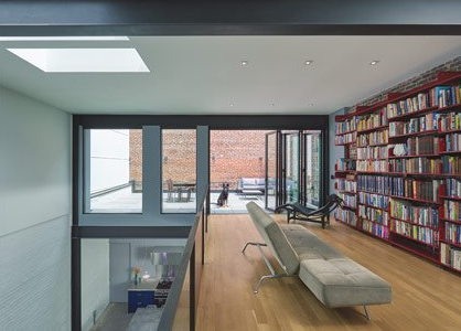 Modern living room with bookshelves, skylight, and large windows overlooking a patio