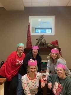 Group of people in pink festive hats posing by a fireplace decorated with stockings.