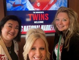 Three smiling people pose at a Minnesota Twins welcome sign