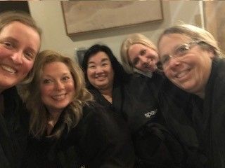 Five smiling people in dark clothing posing closely indoors