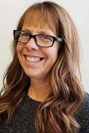 Smiling woman with glasses and long wavy hair against a light background