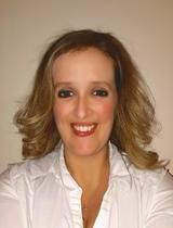 Smiling woman with shoulder-length wavy hair wearing a white blouse against a plain background