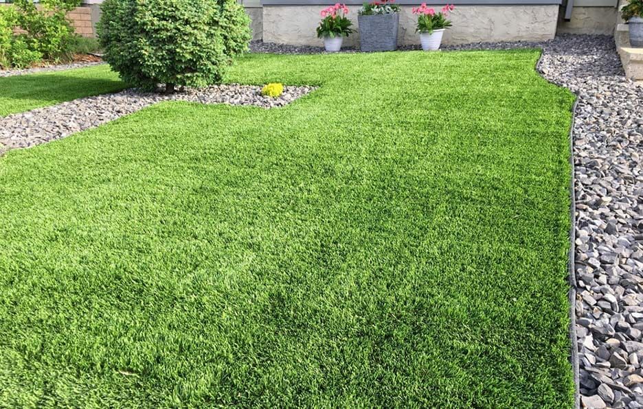 A Lush Green Lawn With Rocks and Flowers in Front of a House — Oaks Quality Turf In Coolangatta, NSW