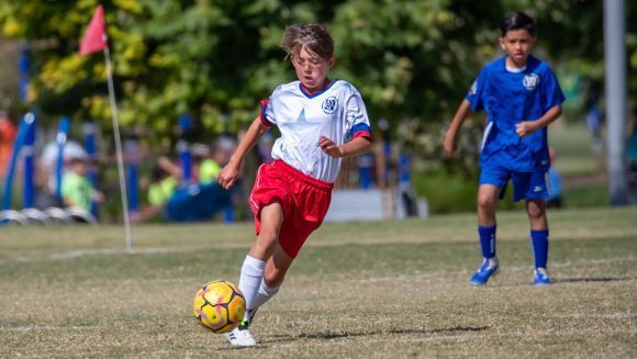 Children in colorful uniforms play a soccer game on an outdoor field.