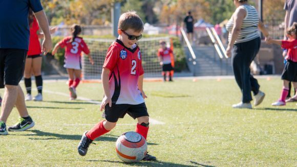 Children in colorful uniforms play a soccer game on an outdoor field.