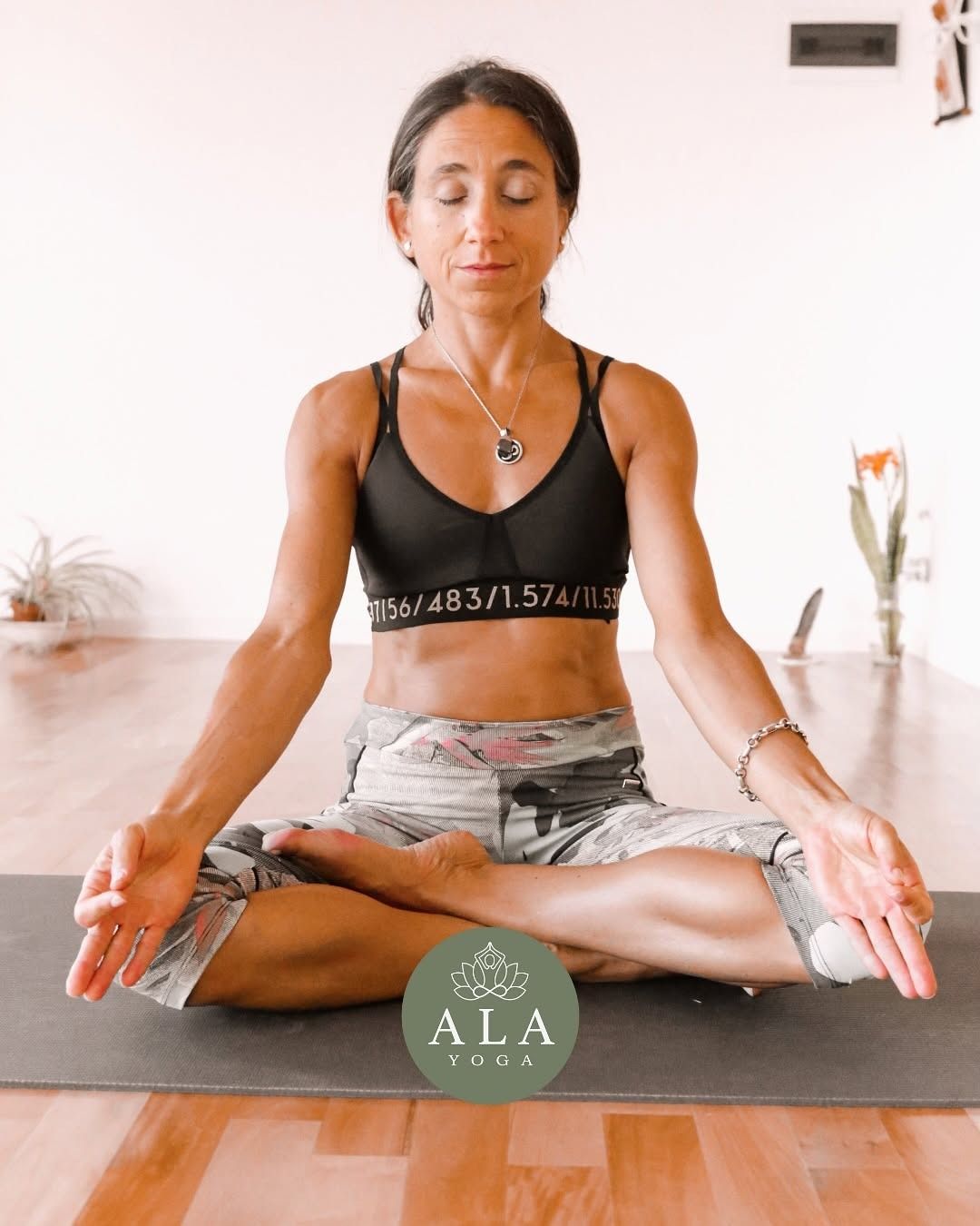 Mujer con ropa deportiva roja haciendo yoga sobre césped verde, con la espalda arqueada y la cabeza erguida.