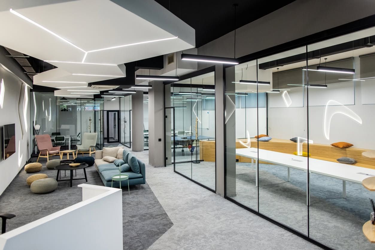 Modern office lounge with glass meeting rooms, gray carpet, and colorful seating area