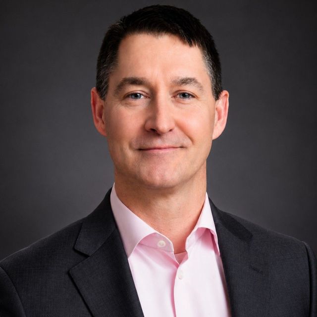 Dave DuRoss Profile Picture - a man in a suit and pink shirt is smiling for the camera .