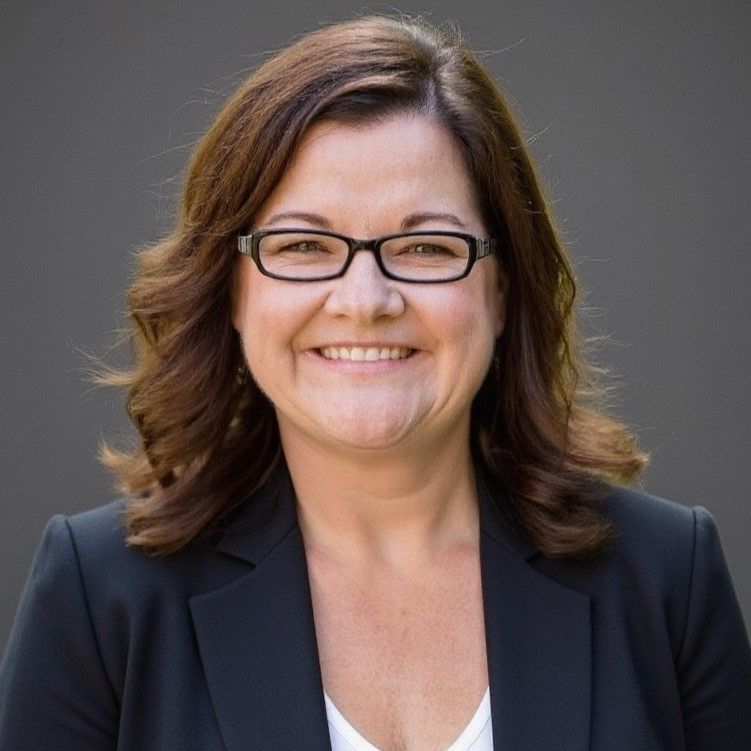 Woman wearing glasses and a black blazer smiles at the camera.
