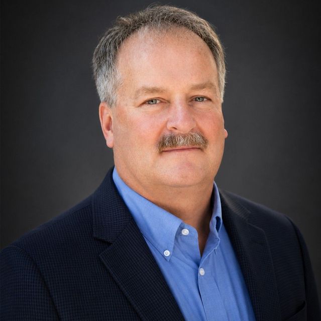 Mark Hueteen Profile Picture - a man with a mustache is wearing a suit and blue shirt .