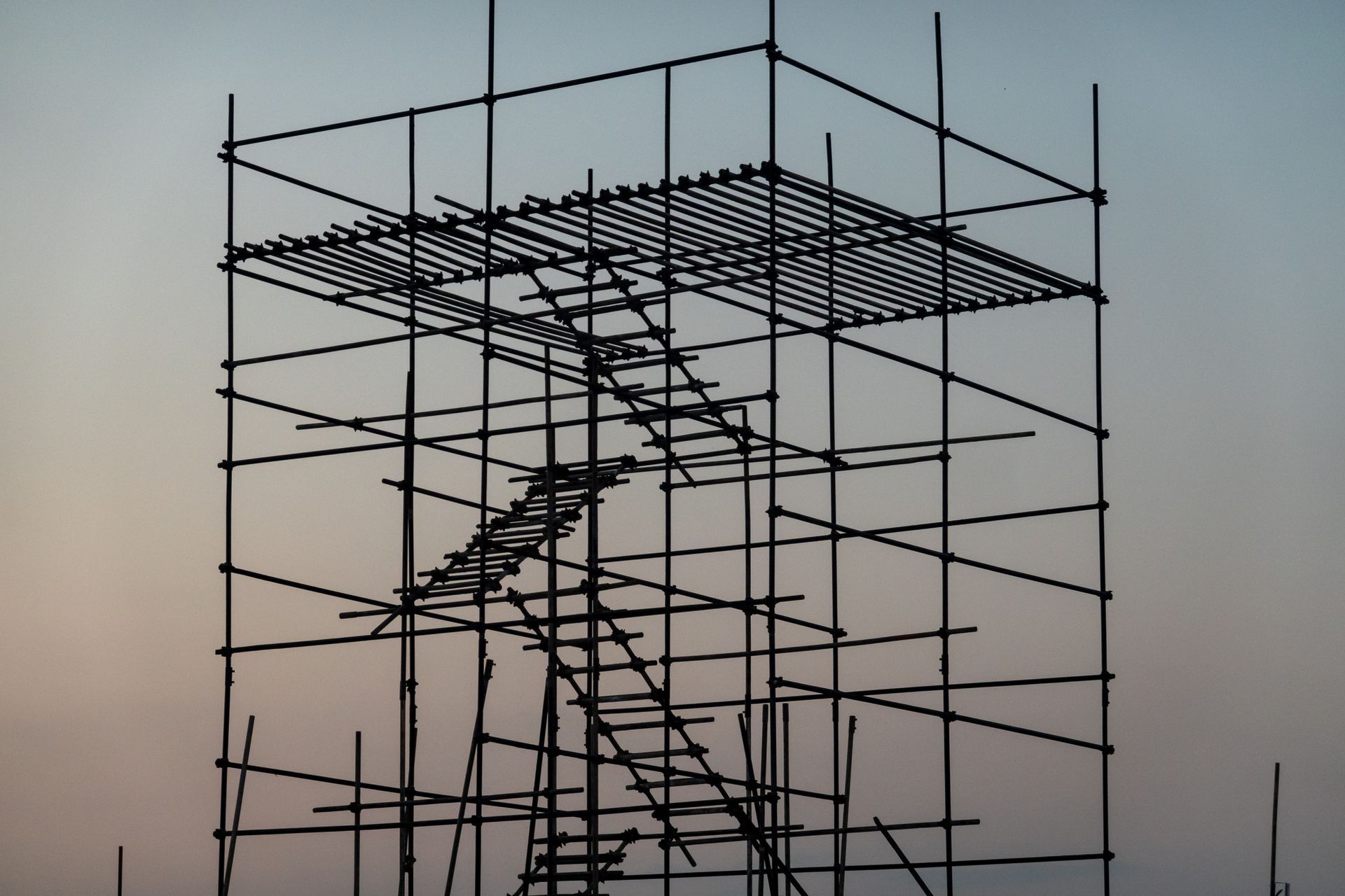 Scaffolding structure silhouetted against a dusky sky, with interior stairs leading to a platform at the top.