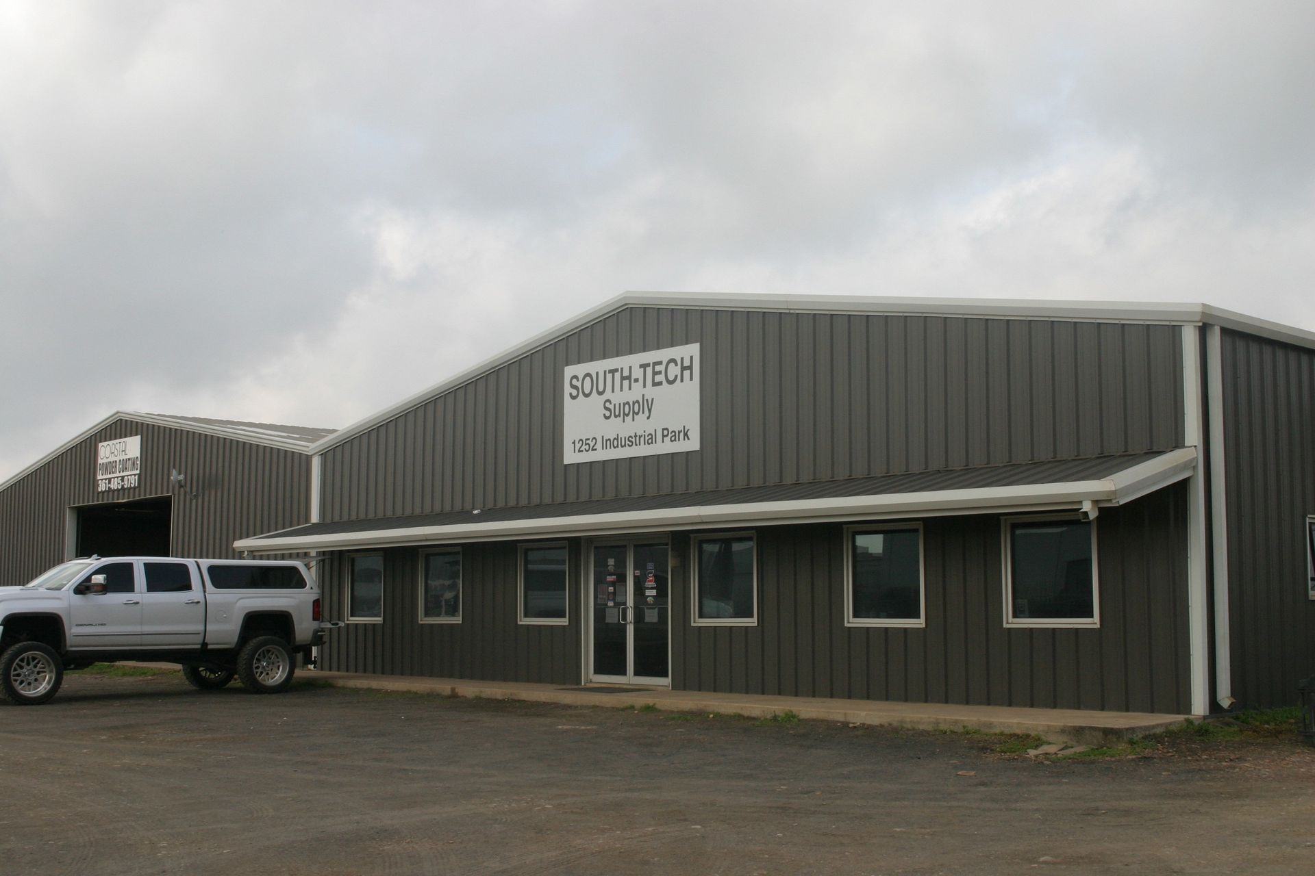 A grey metal industrial warehouse building with a South-Tech Supply sign, featuring a white truck parked in front.